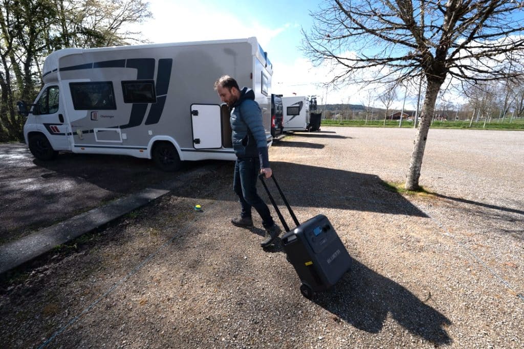 Transport de la batterie nomade Bluetti Elite 400 sur roulettes à côté d’un camping-car