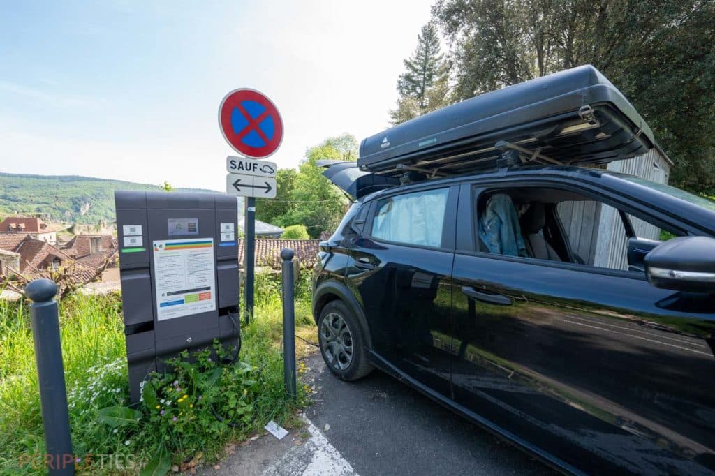 Voiture aménagée électrique stationnée sur un parking de Saint-Cirq-Lapopie dans le Lot