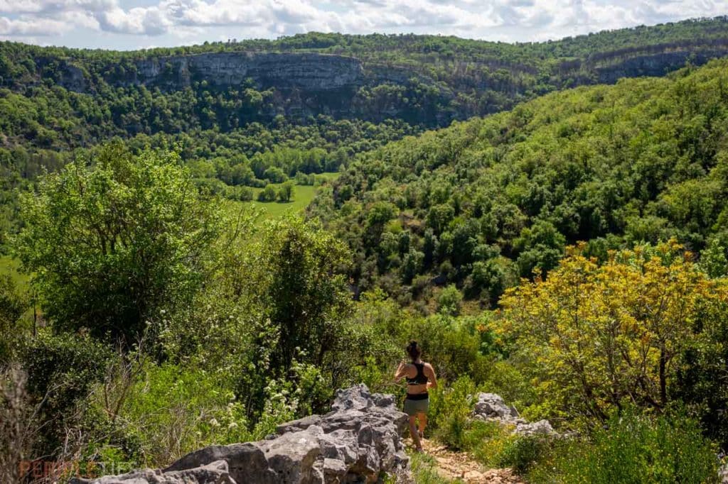 Randonneur sur un rocher avec vue sur la vallée du Célé verdoyante dans le Lot