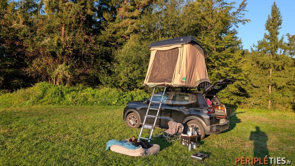 Tente de toit dépliée sur une voiture électrique dans un pré en Slovénie